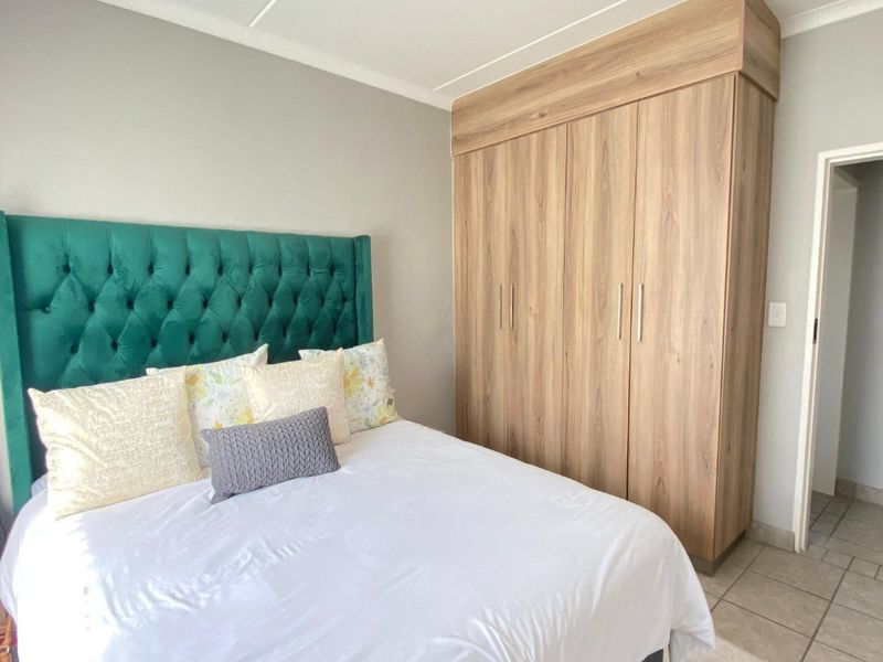 A well-maintained bedroom featuring a large built-in wooden wardrobe, tiled flooring, and a modern ceiling light fixture.