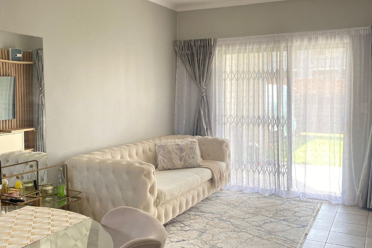 A bright living room featuring neutral tiled flooring, a coved ceiling, and a large sliding glass door with a security gate leading to the outdoors.