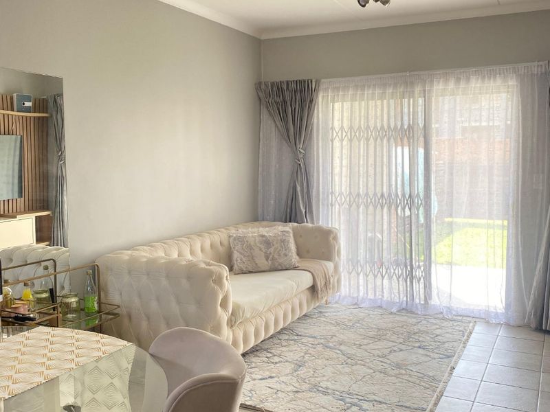 A bright living room featuring neutral tiled flooring, a coved ceiling, and a large sliding glass door with a security gate leading to the outdoors.
