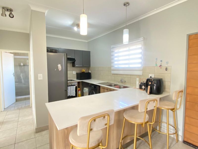 Modern open-plan kitchen featuring sleek cabinetry, stone countertops, a breakfast bar, and integrated appliances, seamlessly flowing into the living area.