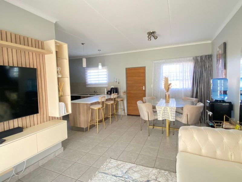 A bright open-plan living and dining area featuring tiled floors, a modern kitchen island, and a custom slatted wood media wall.