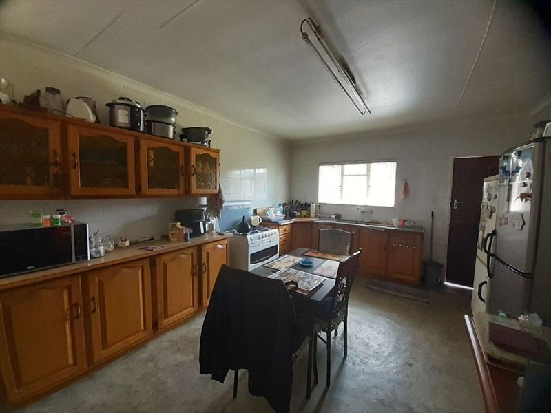A functional kitchen featuring traditional wooden cabinetry, laminate countertops, a freestanding stove, and a double sink, offering potential for modern renovation.