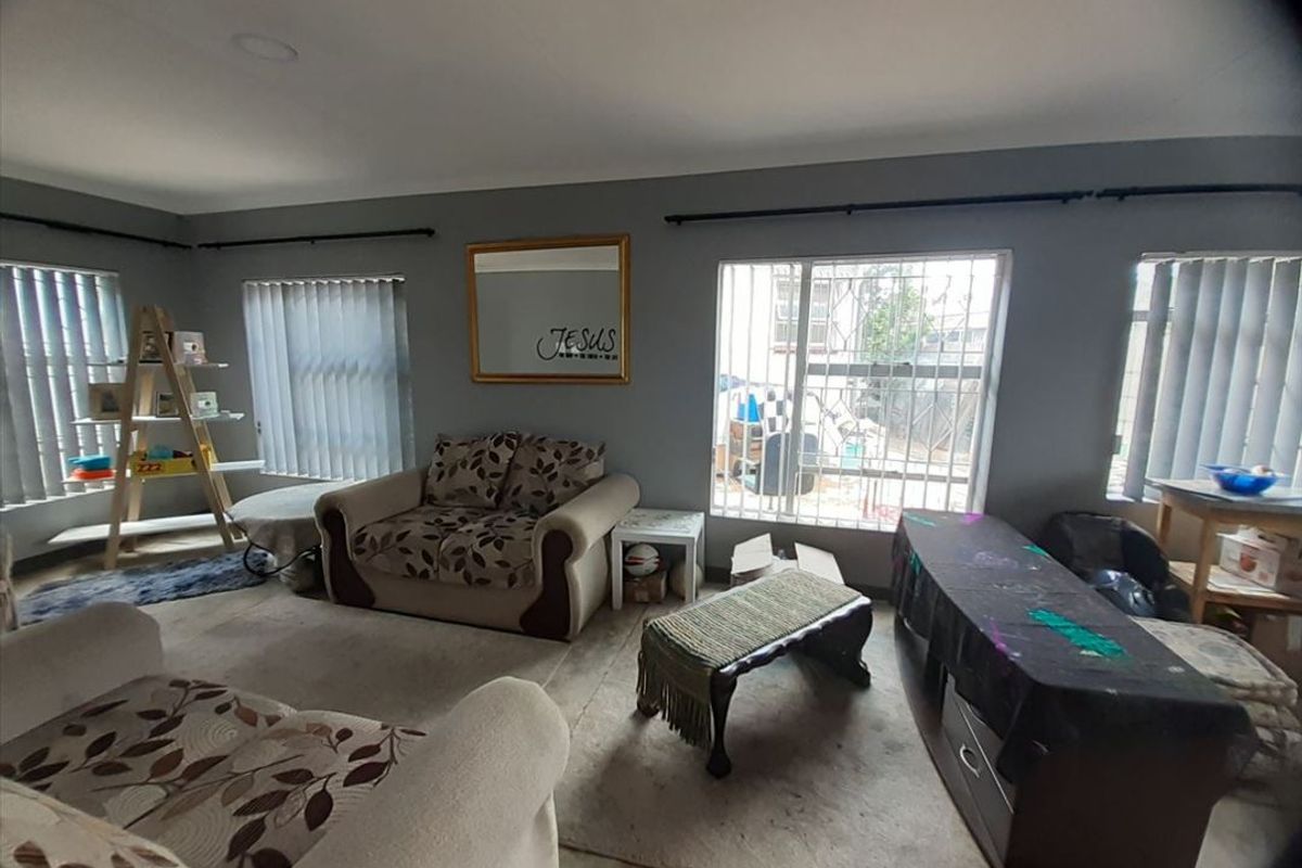 A living room featuring grey walls, security bars on windows, and vertical blinds, requiring cosmetic updates to improve the overall aesthetic.