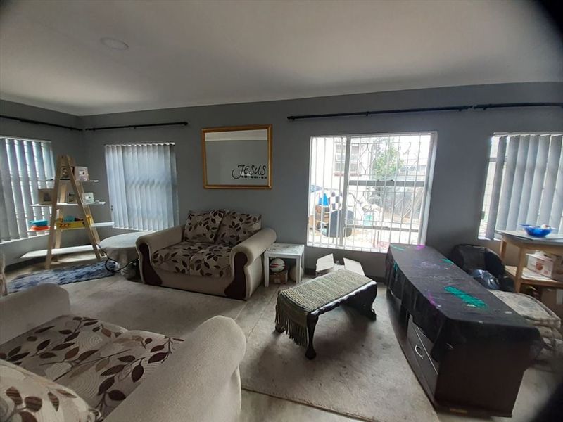 A living room featuring grey walls, security bars on windows, and vertical blinds, requiring cosmetic updates to improve the overall aesthetic.