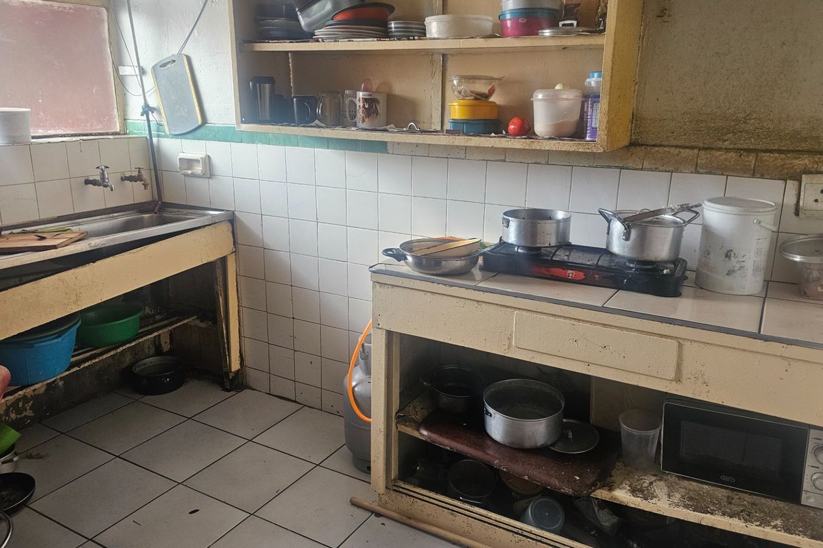 A dated kitchen area featuring tiled splashbacks, built-in cabinetry, and a stainless steel sink, requiring significant refurbishment and modernization.