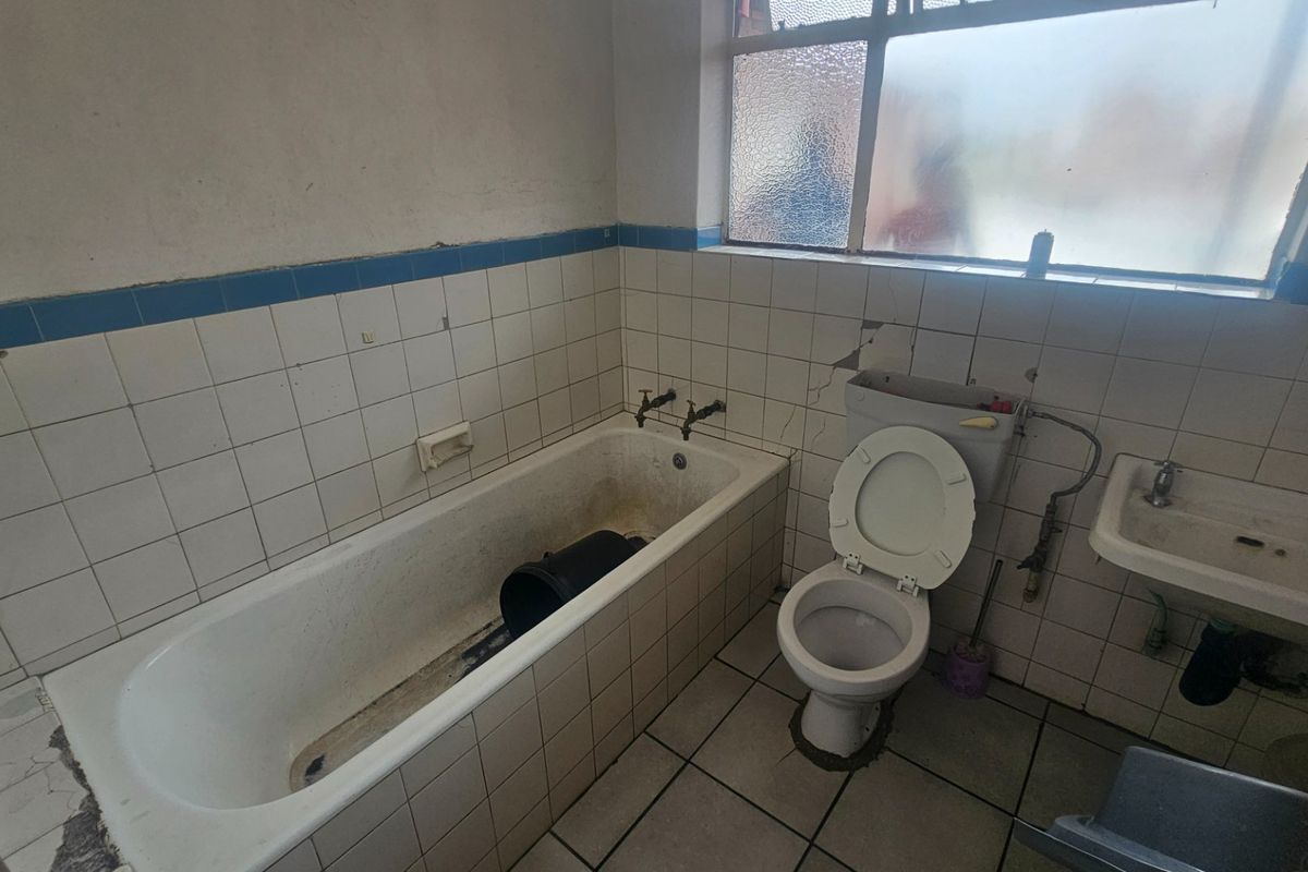 A dated bathroom featuring a built-in bathtub, toilet, and wall-mounted basin, requiring significant renovation and repair to the wall tiles and finishes.