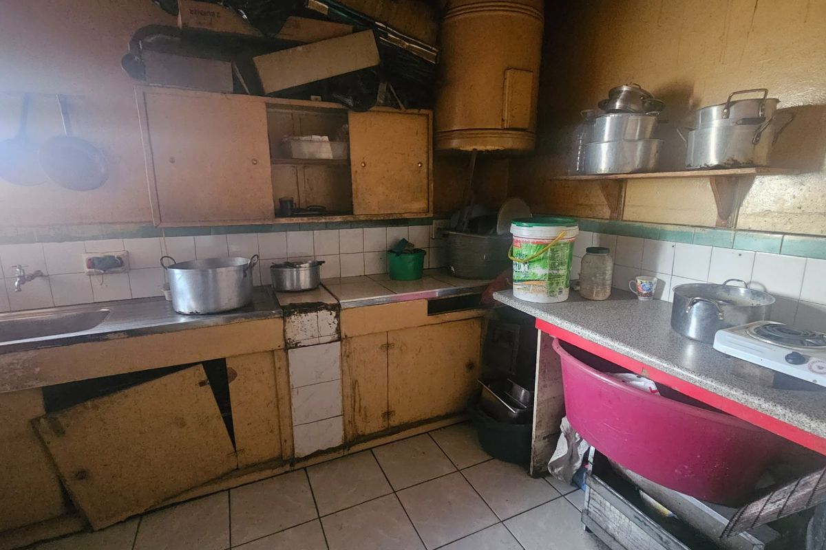 A dated kitchen featuring original cabinetry, tiled splashbacks, and a stainless steel sink, requiring significant renovation and modernization of fixed finishes.