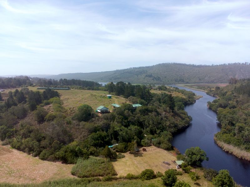 An aerial view of a farm property featuring multiple dwellings situated on a hillside overlooking a river and surrounding natural landscape.