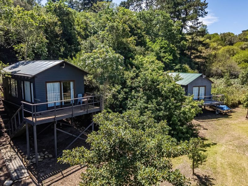 Aerial view of two elevated timber cabins nestled in a lush, wooded farm setting, featuring private decks and metal roofing.