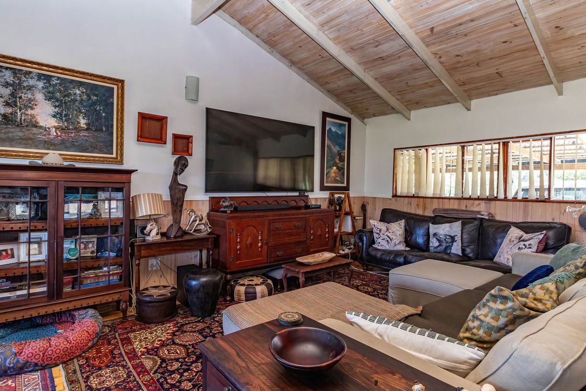 A cozy living room featuring exposed timber beam ceilings, warm timber wall paneling, and horizontal windows that provide natural light.