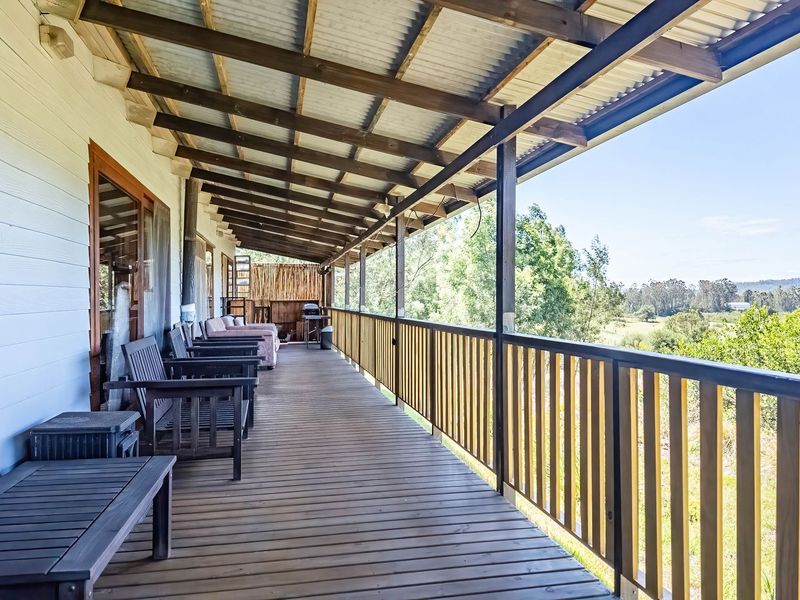 A spacious covered timber veranda featuring exposed rafters and a wooden balustrade, offering expansive views of the surrounding farm landscape.