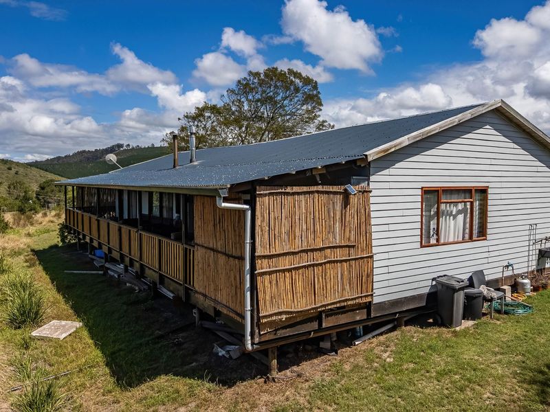 Rear view of a farm dwelling featuring corrugated metal roofing, timber cladding, and an elevated deck area with bamboo privacy screening.