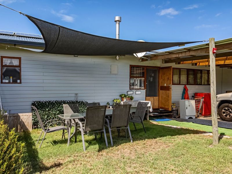 Rear exterior view of the farm property featuring a shade sail, carport, and timber-clad facade with a flue pipe.