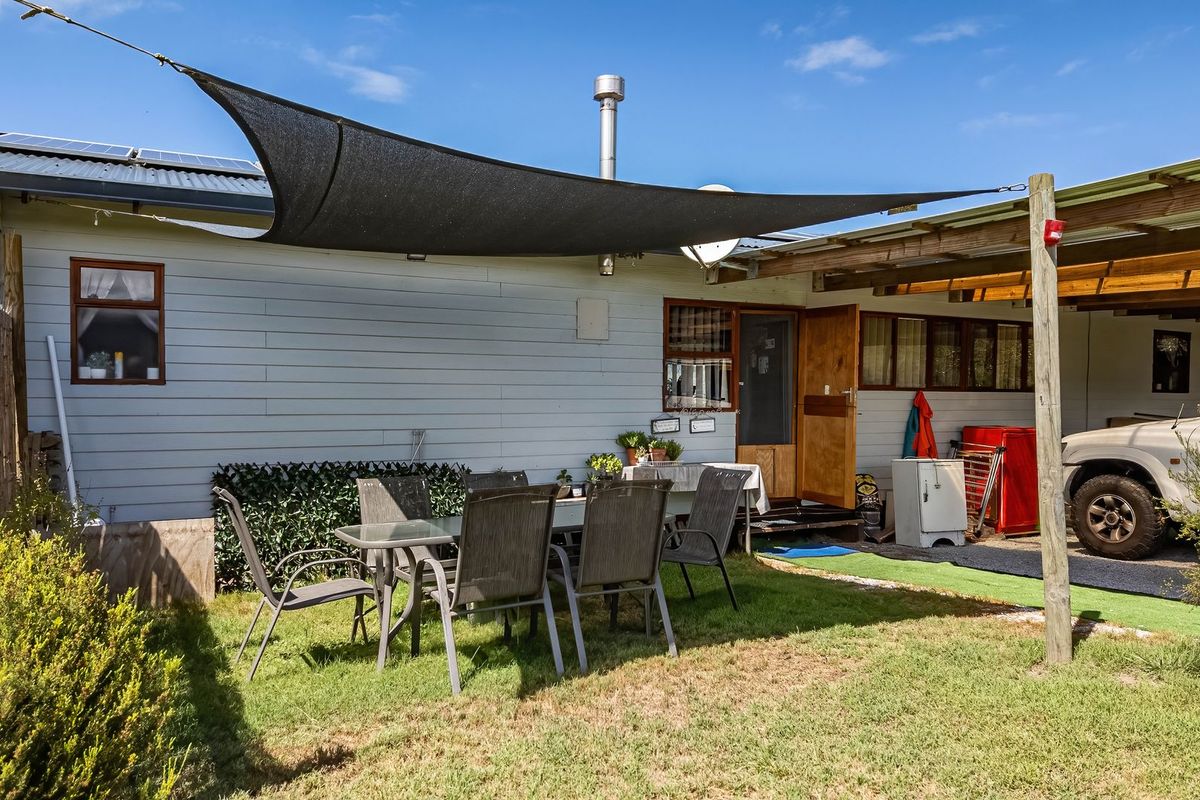 Rear exterior view of the farm property featuring a shade sail, carport, and timber-clad facade with a flue pipe.