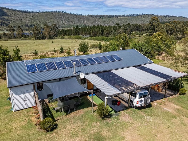 Aerial view of a farm dwelling featuring a corrugated metal roof with extensive solar panel installation and an attached carport structure.
