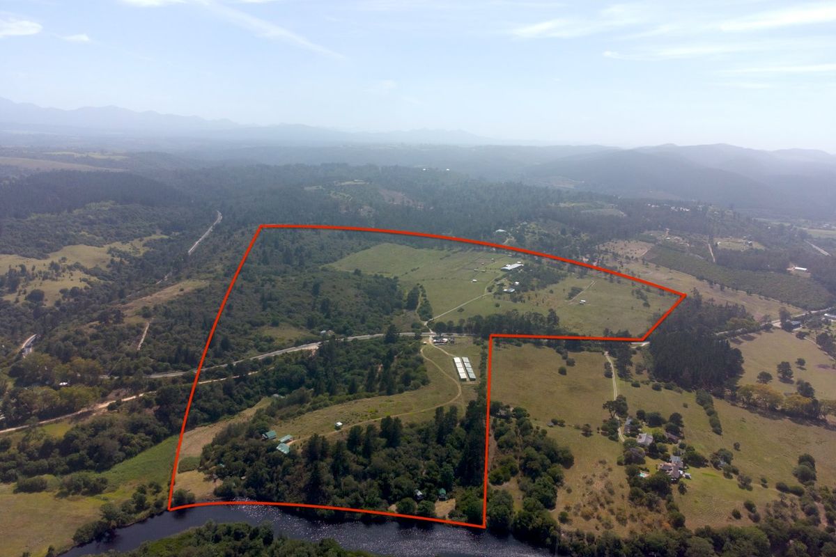 An aerial view of a large farm property featuring extensive agricultural land, natural woodland, and direct river frontage within a rural landscape.