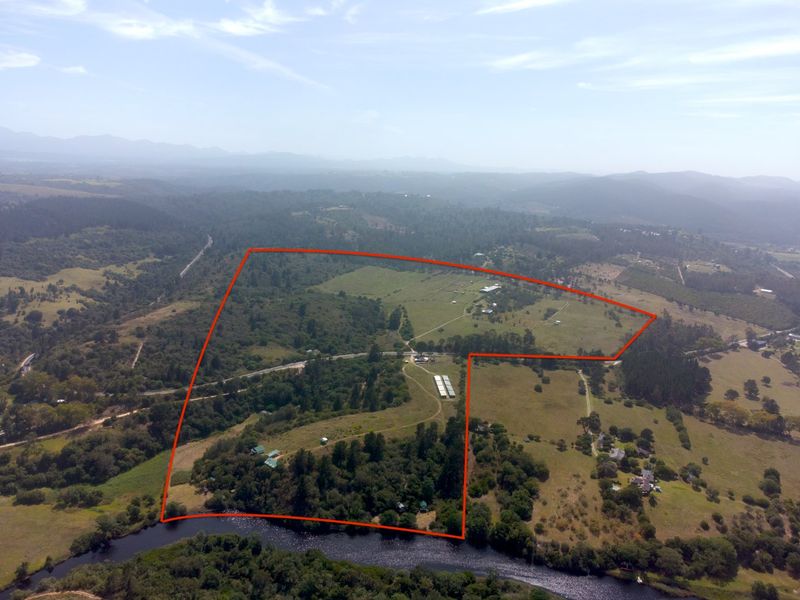 An aerial view of a large farm property featuring extensive agricultural land, natural woodland, and direct river frontage within a rural landscape.