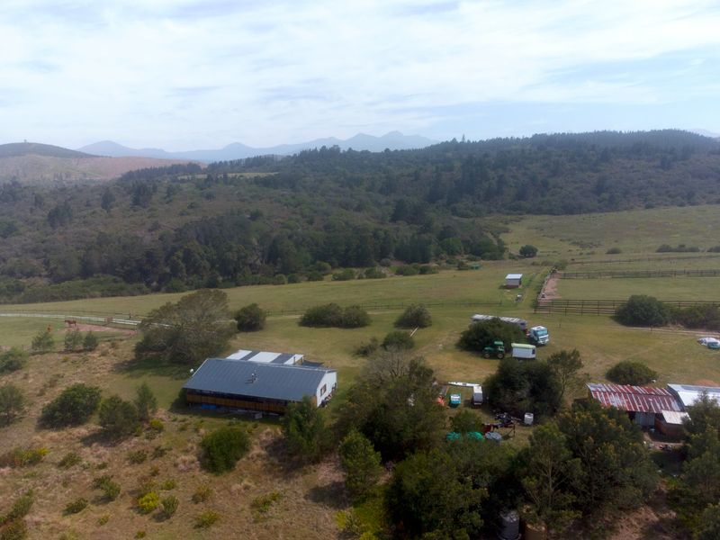 Aerial view of the farm property featuring the main dwelling, outbuildings, fenced paddocks, and expansive surrounding landscape.