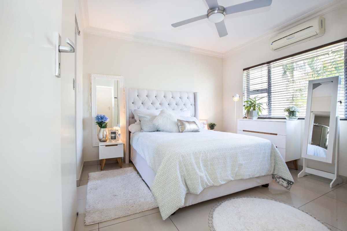 A well-maintained bedroom featuring tiled flooring, a ceiling fan, and a wall-mounted split-system air conditioner for climate control.
