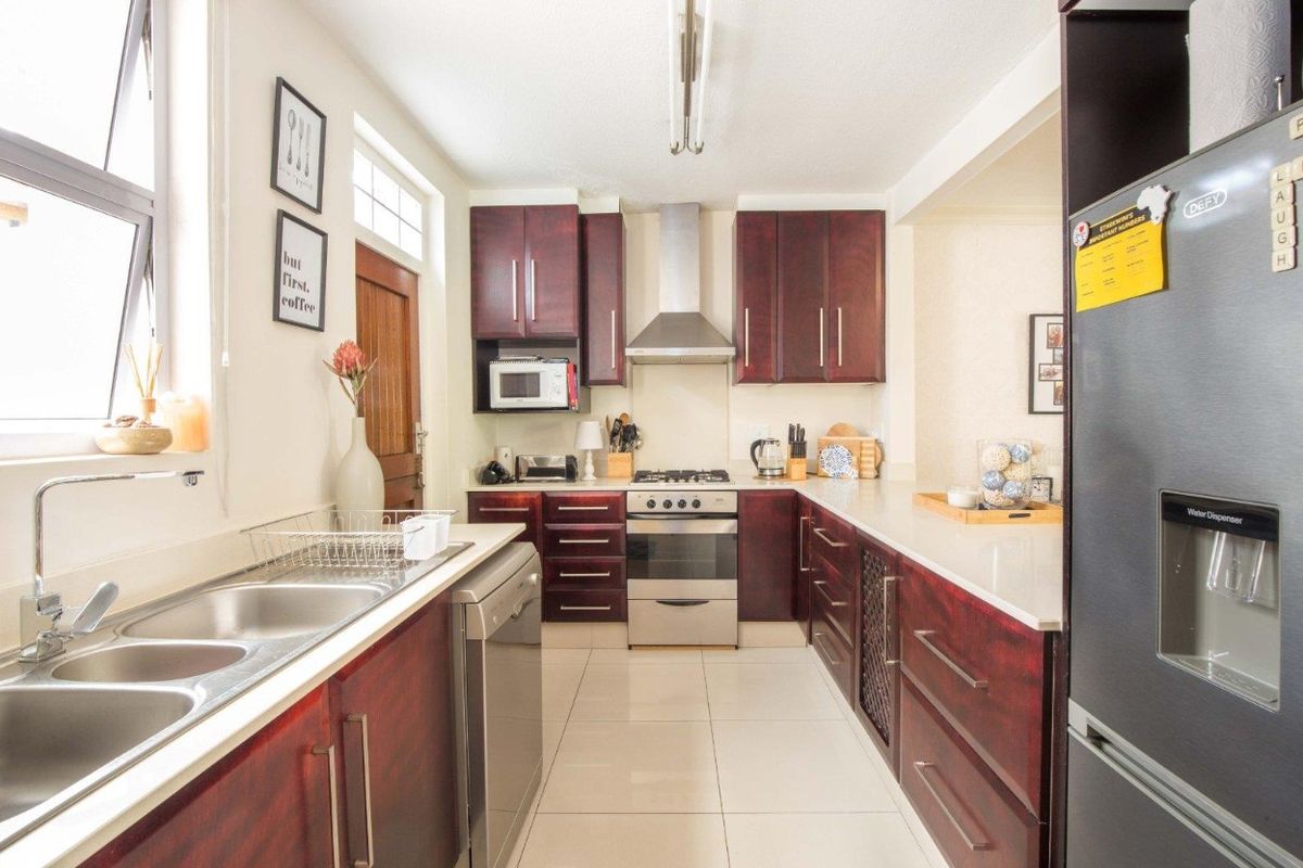 A functional kitchen featuring dark wood cabinetry, stone countertops, a gas stove with extractor fan, and tiled flooring.