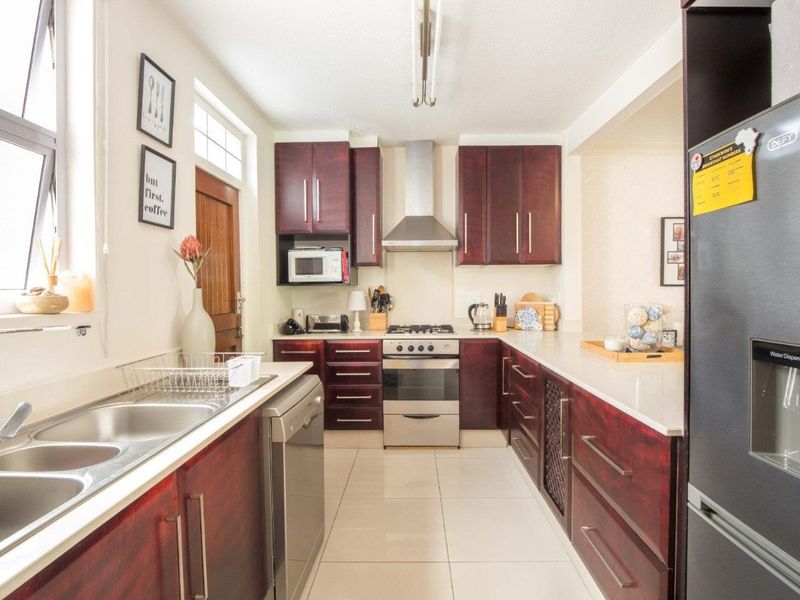 A functional kitchen featuring dark wood cabinetry, stone countertops, a gas stove with extractor fan, and tiled flooring.