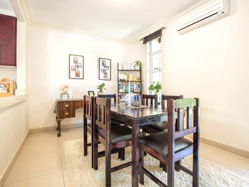 A bright dining area featuring tiled flooring, coving, and a wall-mounted split-system air conditioner, adjacent to the kitchen space.
