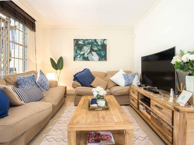 A comfortable living room featuring tiled flooring, crown molding, and a security gate on the window.