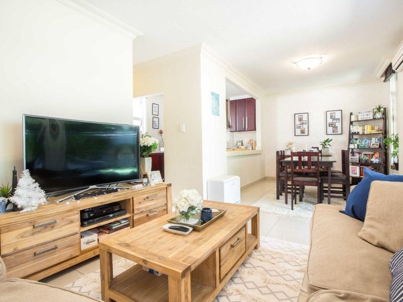 An open-plan living and dining area featuring tiled flooring, neutral walls, and a connected kitchen space with built-in cabinetry.