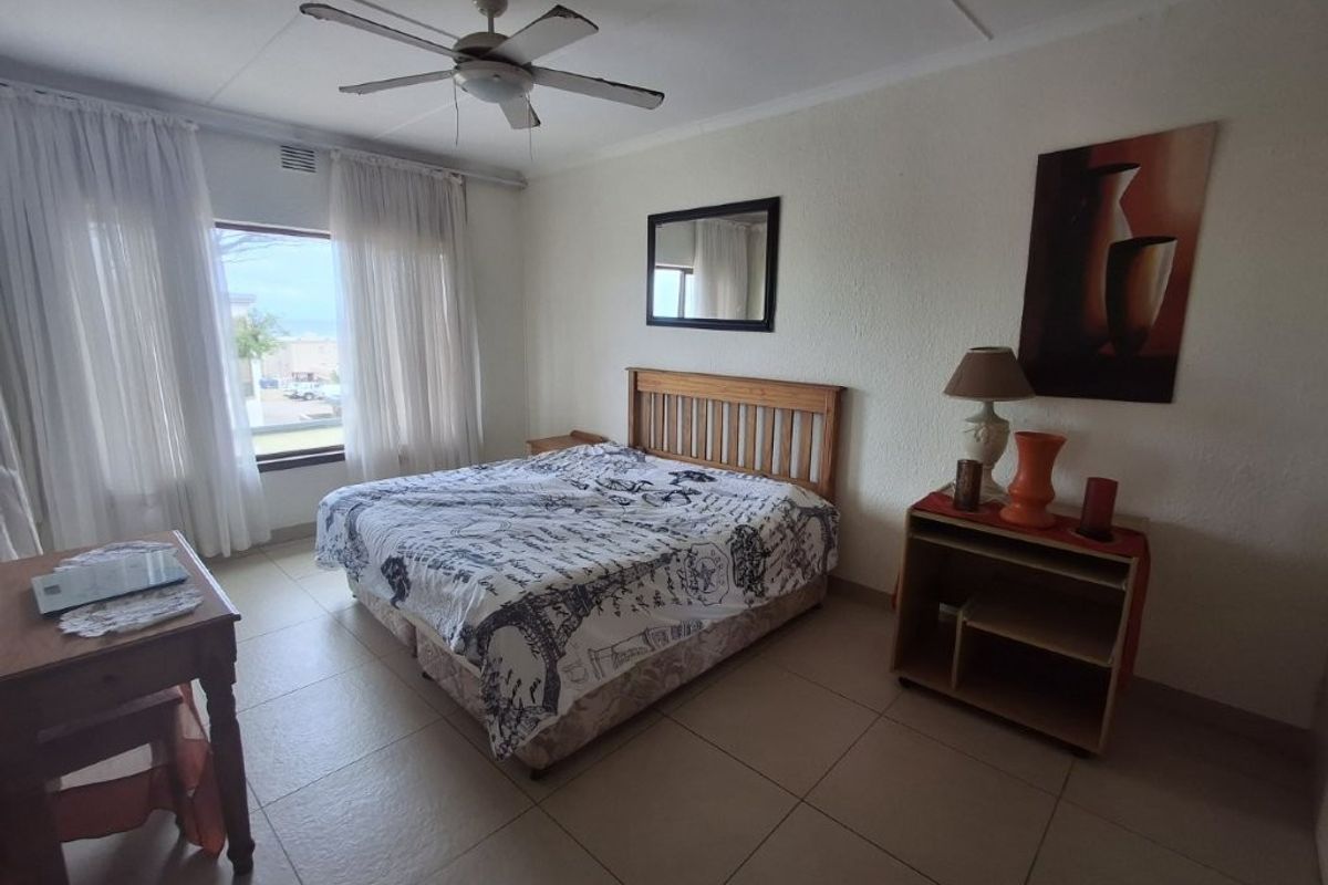 A spacious bedroom featuring tiled flooring, a ceiling fan, and a large window that allows for natural light.