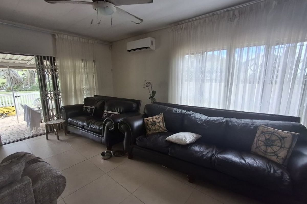 A living room featuring tiled flooring, a ceiling fan, and a wall-mounted air conditioning unit, with direct access to an outdoor patio area.
