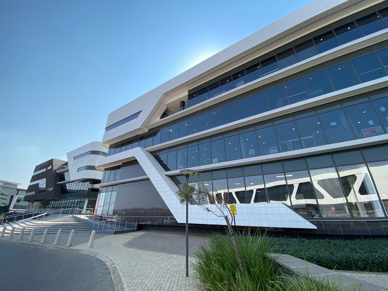 Modern commercial office building featuring extensive glass curtain walling, contemporary composite panel cladding, and paved pedestrian access with integrated stairs and bollards.