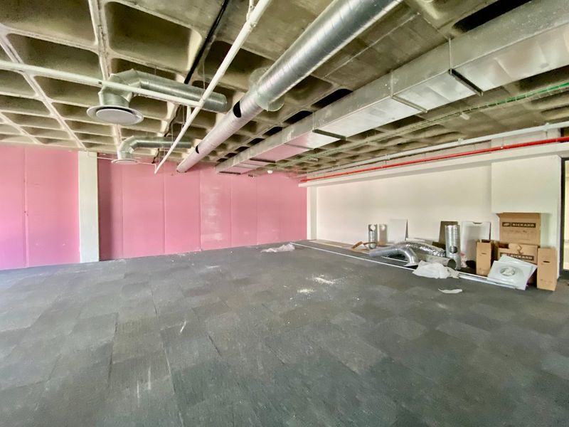 An open-plan commercial space featuring an exposed waffle slab ceiling, industrial HVAC ducting, and carpet tile flooring, currently in a shell condition.
