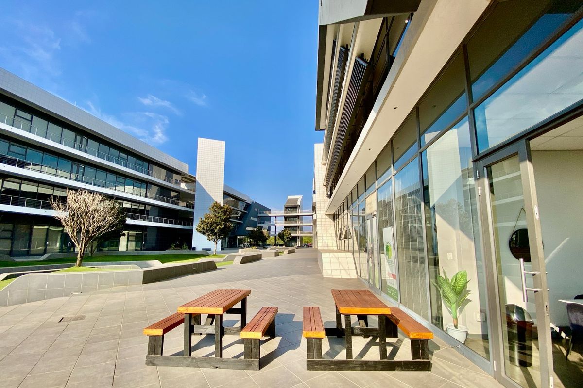 Modern commercial office complex featuring a spacious paved courtyard, glass facade architecture, and landscaped outdoor areas for professional use.
