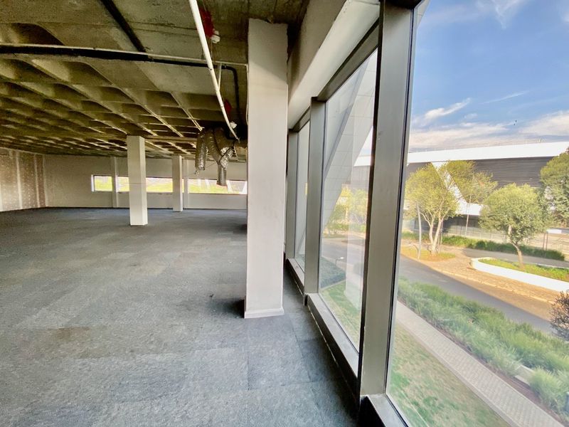 An expansive, open-plan commercial office space featuring an exposed concrete waffle ceiling, large glass windows, and industrial-style exposed ducting.