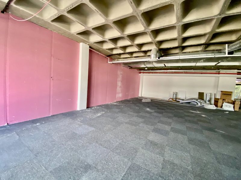 An open-plan commercial space featuring an exposed waffle slab ceiling, industrial ductwork, and grey carpet tiles, currently in a shell condition.