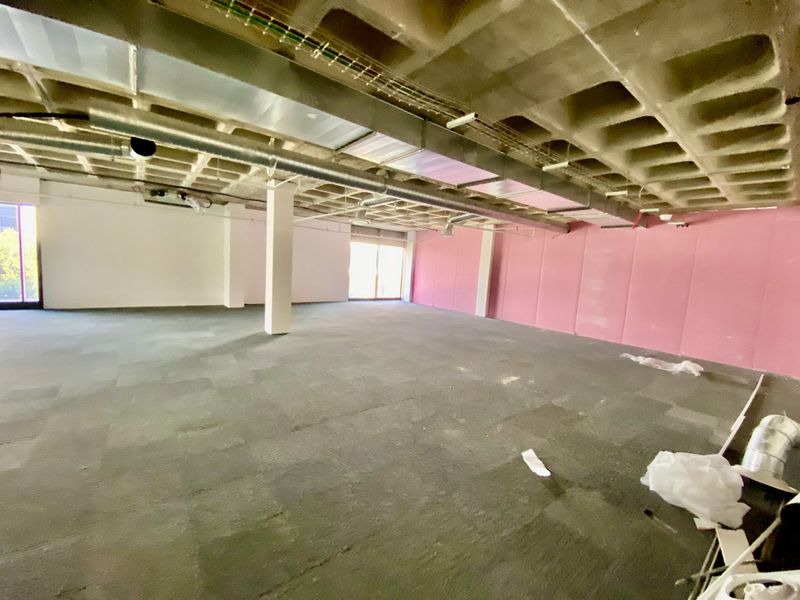 An expansive, open-plan commercial office space featuring an exposed waffle slab ceiling, industrial HVAC ducting, and carpet tile flooring.
