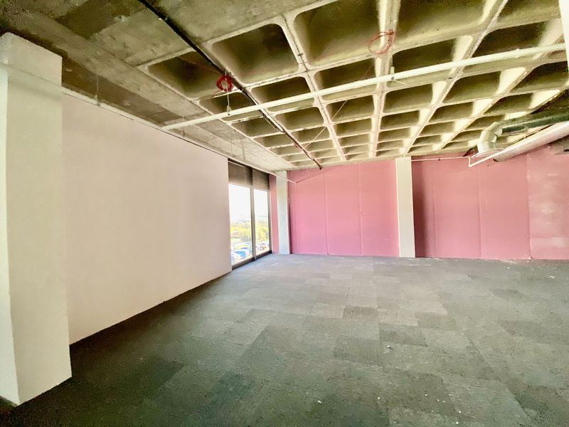 An empty commercial office space featuring an exposed waffle slab concrete ceiling, carpeted flooring, and large windows providing natural light.