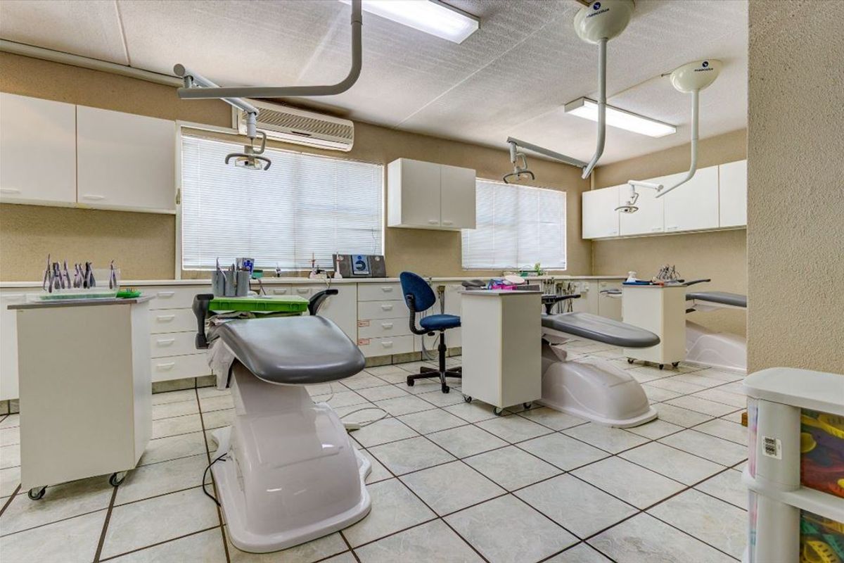 A functional commercial dental or medical treatment room featuring built-in cabinetry, tiled flooring, and overhead clinical lighting fixtures.