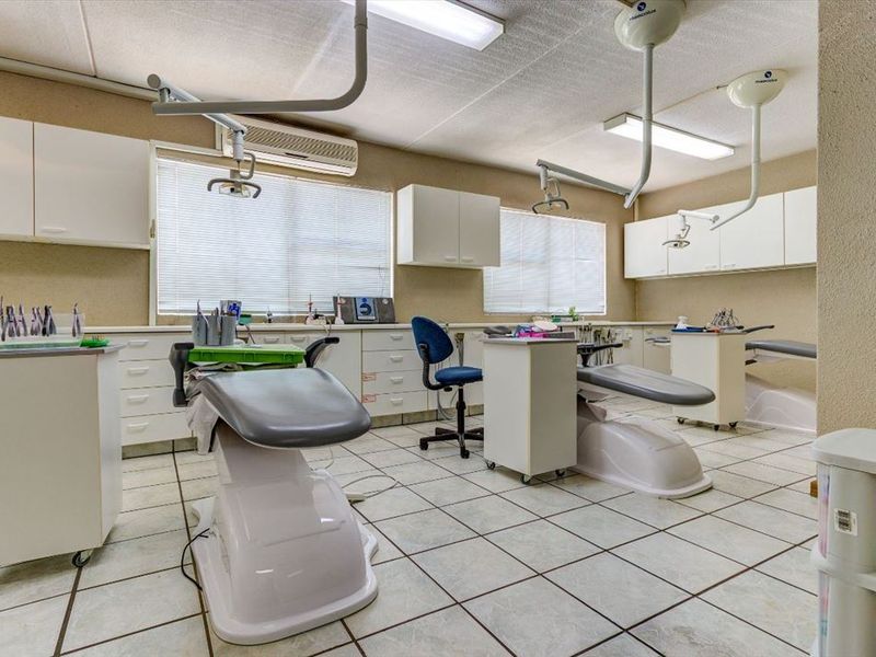 A functional commercial dental or medical treatment room featuring built-in cabinetry, tiled flooring, and overhead clinical lighting fixtures.