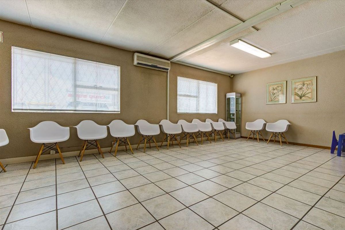 A commercial waiting area or office space featuring tiled flooring, fluorescent lighting, and a wall-mounted air conditioning unit.