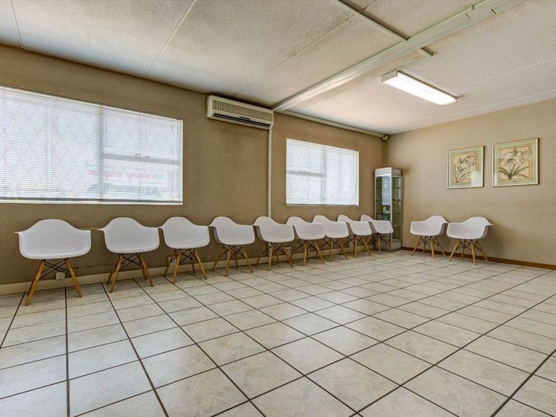 A commercial waiting area or office space featuring tiled flooring, fluorescent lighting, and a wall-mounted air conditioning unit.