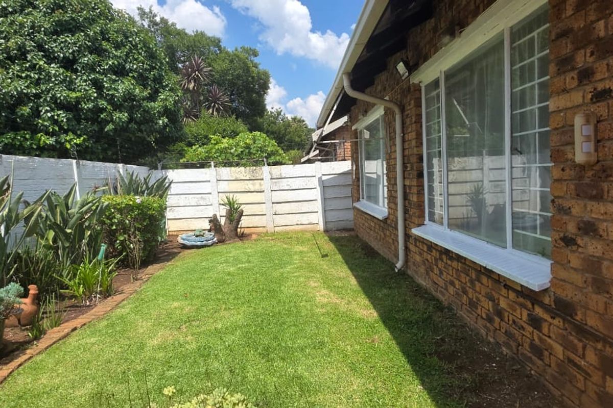 A private rear garden featuring a well-maintained lawn, established perimeter landscaping, and a classic face brick exterior wall with security-fitted windows.