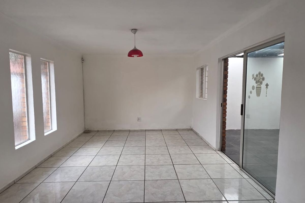An empty, neutrally painted living room featuring ceramic floor tiles, a sliding glass door leading to an adjacent space, and a central pendant light.