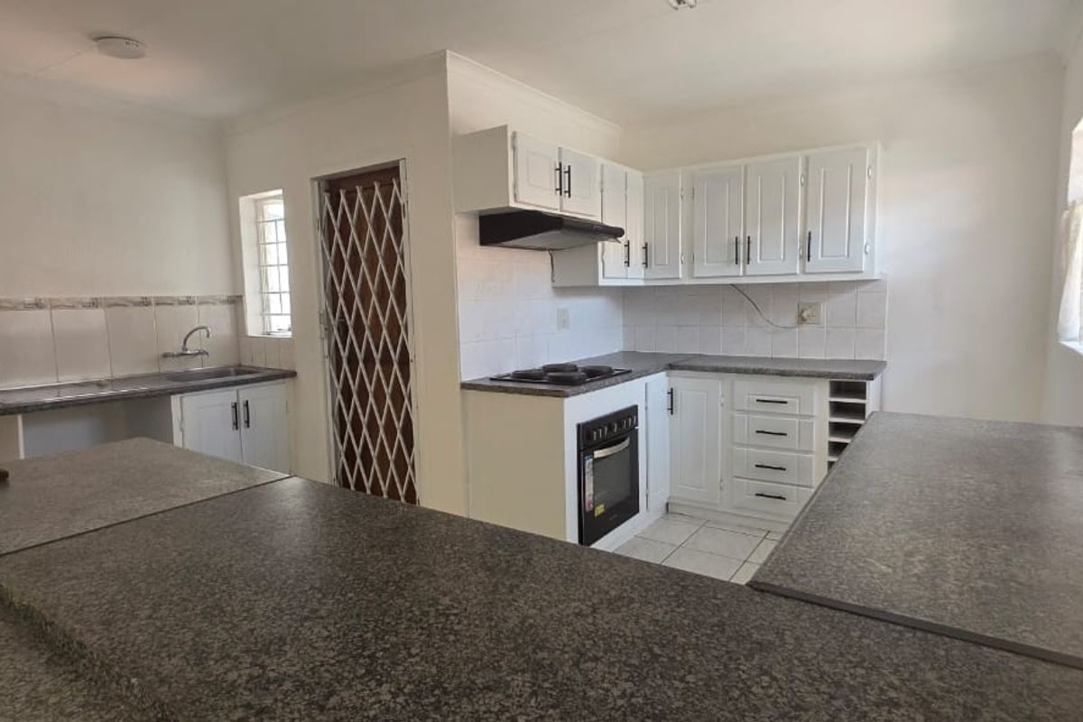 A functional kitchen featuring white cabinetry, laminate countertops, built-in oven, hob, and extractor fan, with a breakfast bar and security gate access.