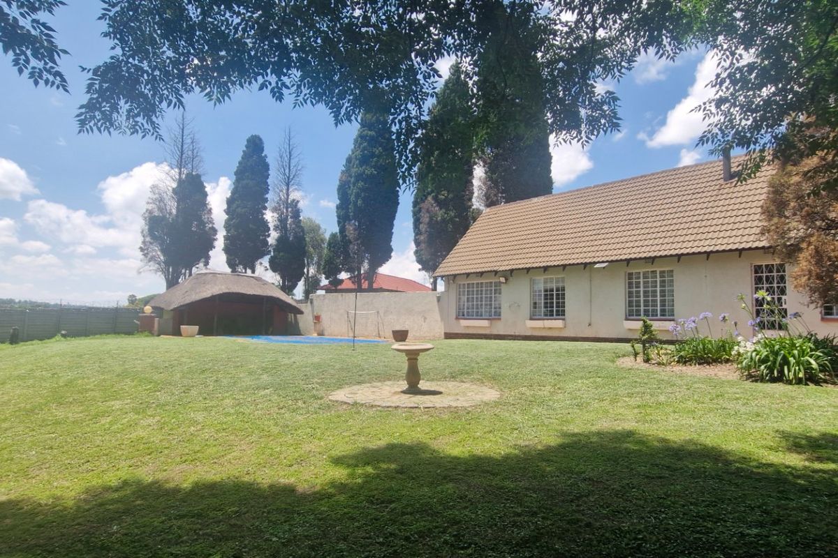 Spacious rear garden featuring a swimming pool, a traditional thatched lapa, and a well-maintained lawn area adjacent to the main house.