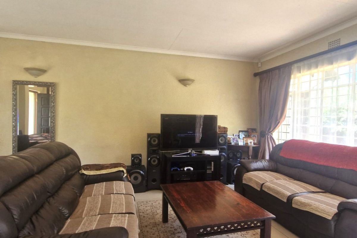 A spacious living room featuring neutral walls, coving, and a large window with security bars, providing ample natural light.