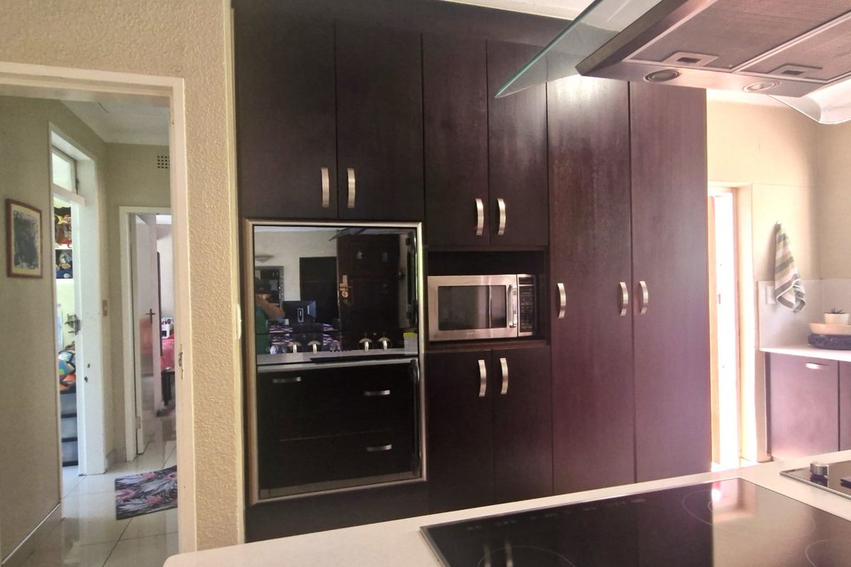 A functional kitchen featuring dark wood cabinetry, built-in oven and microwave, glass extractor fan, and a central island with a hob.