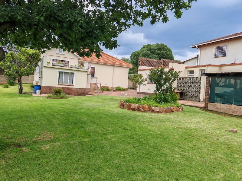 Spacious rear garden featuring a well-maintained lawn, brick paved patio area, and established garden beds with stone edging.
