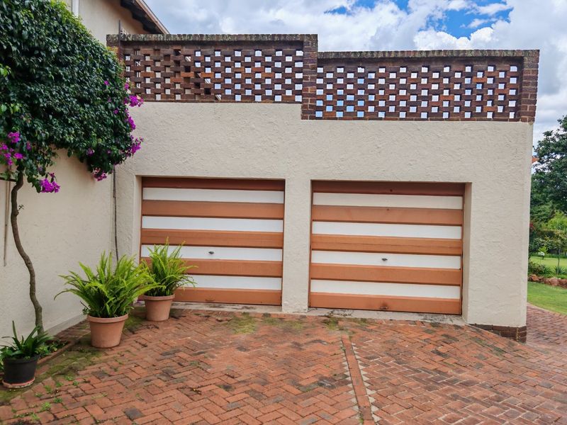 A double garage featuring striped doors and a decorative brick screen wall, set against a paved driveway with established garden greenery.