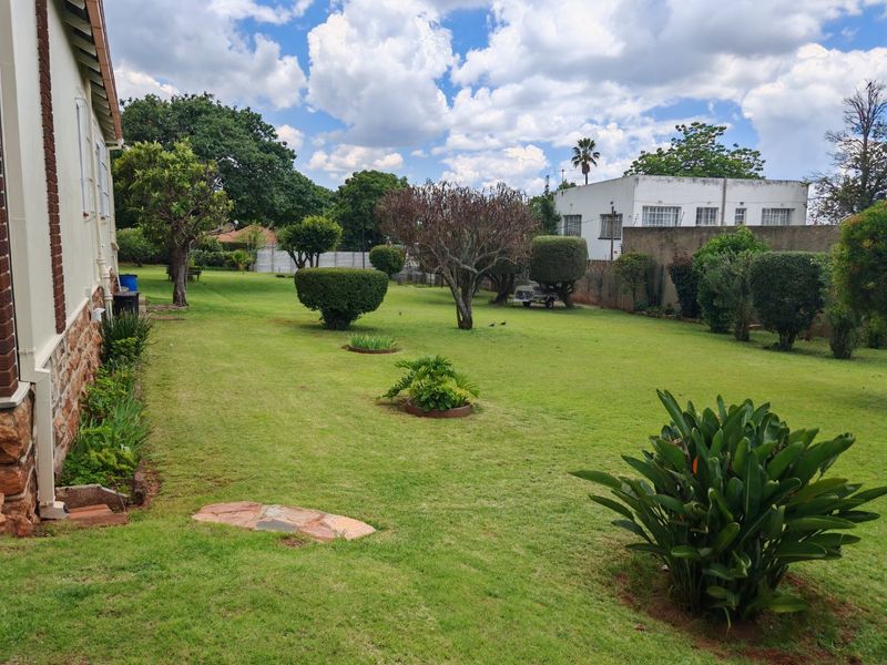 A spacious, well-maintained rear garden featuring a large lawn, mature trees, and established boundary walls.